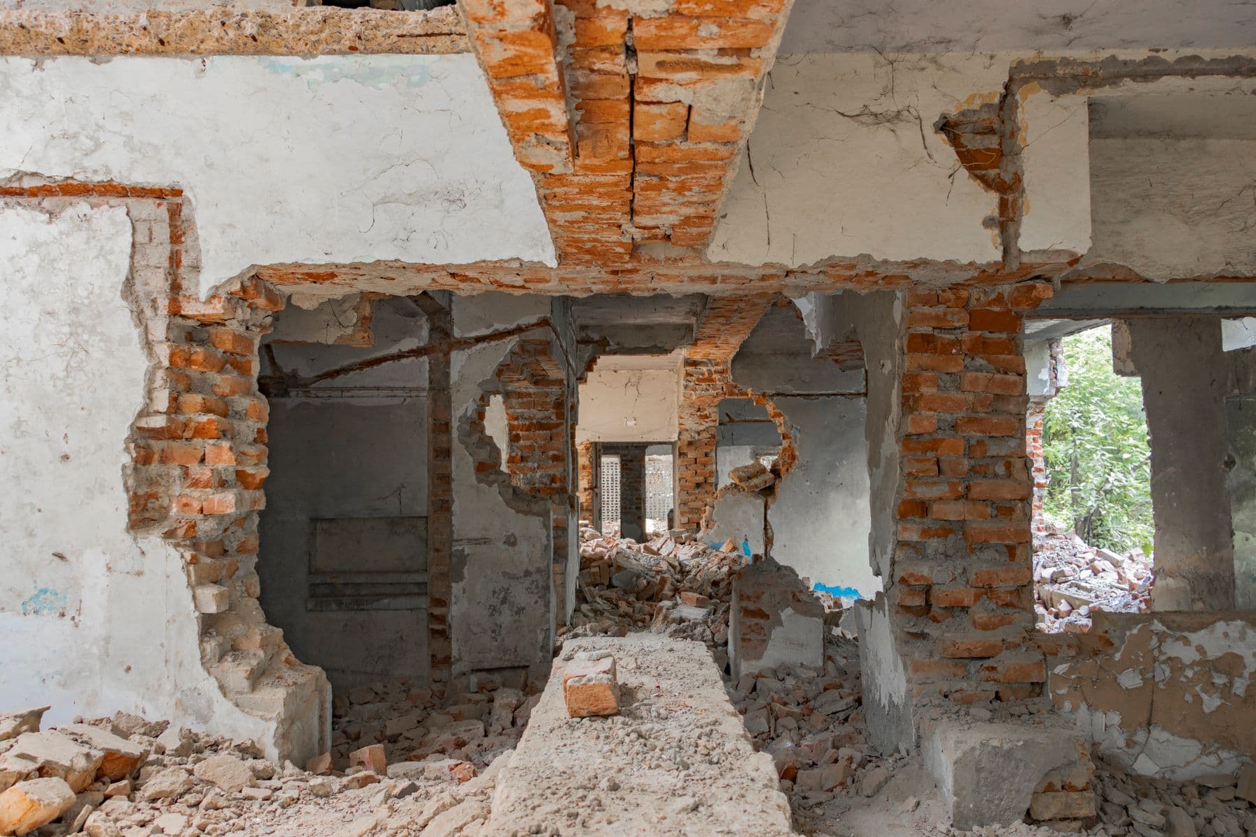 Brick interior walls broken open, with rubble on the floor and daylight through a far window.
