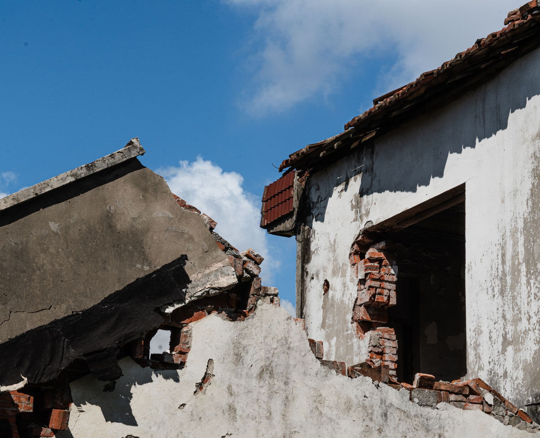 A broken masonry wall with plaster peeling away, open to a blue sky.