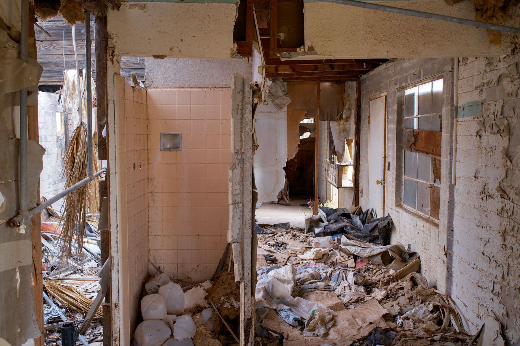 A gutted hallway with tiled walls, open doorways and debris piled on the floor.