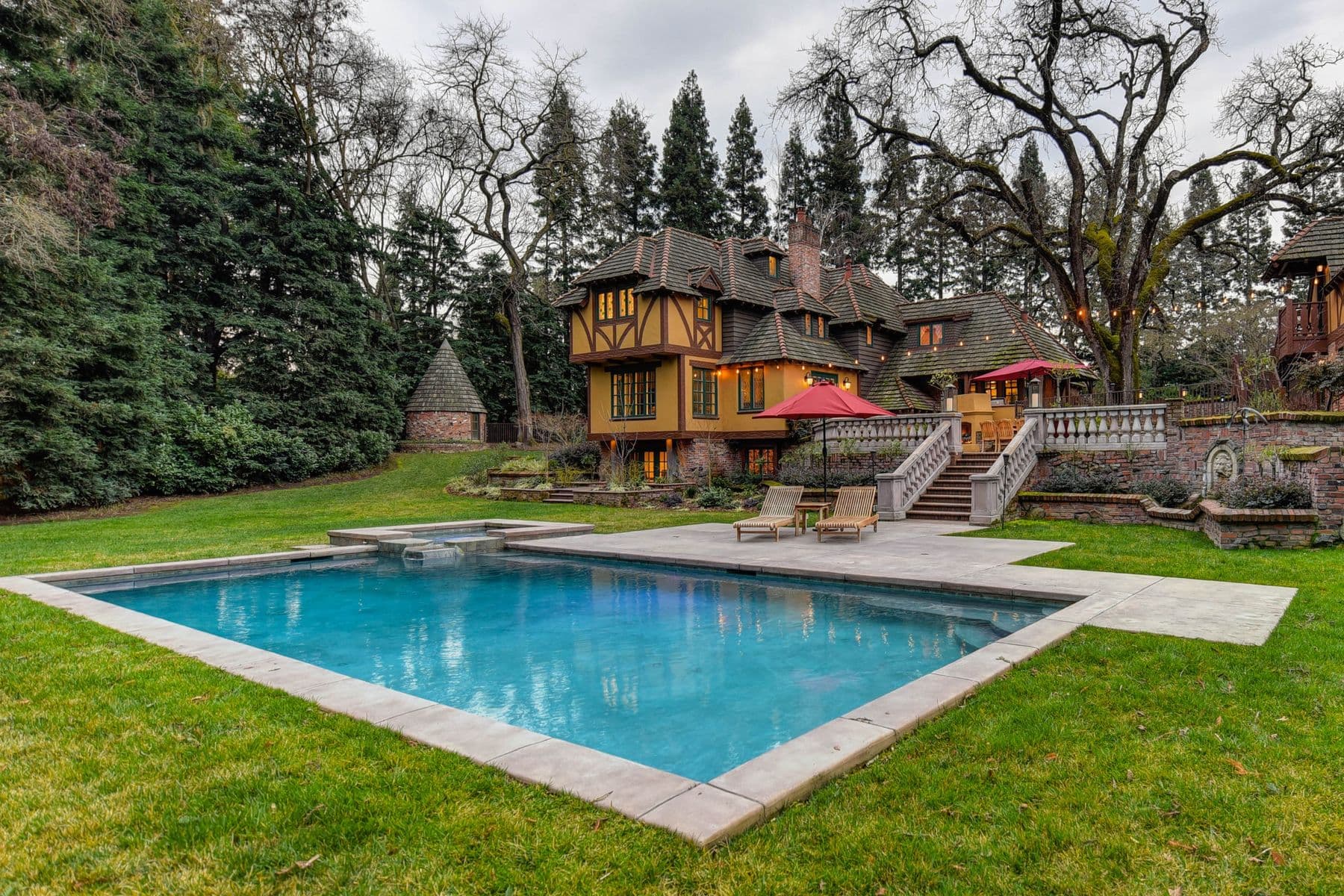 A rectangular swimming pool set in a lawn, with a large house and trees behind it.