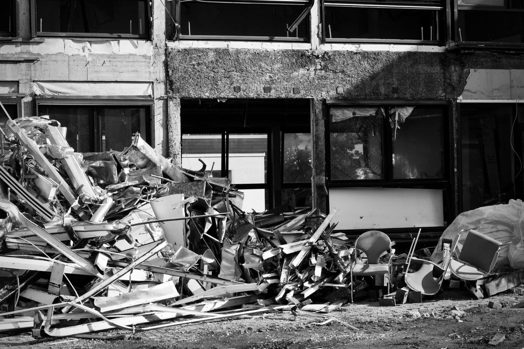 A black-and-white photo of twisted metal debris piled against the front of a gutted building.
